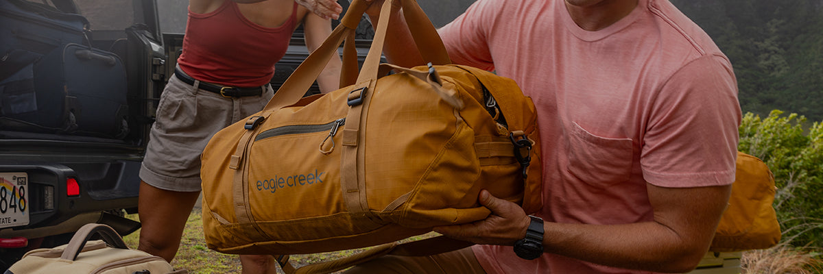 Man packing a carry on duffel bag, travel duffel bag into a car trunk for an outdoor adventure, featuring Eagle Creek branding.